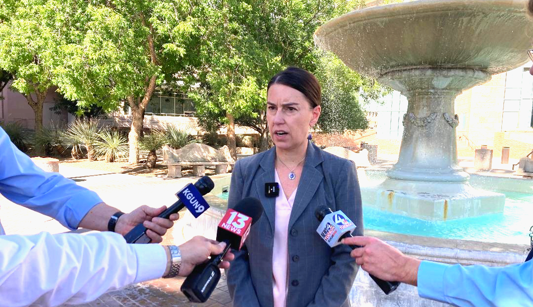a woman stands in front of a gaggle of reporters