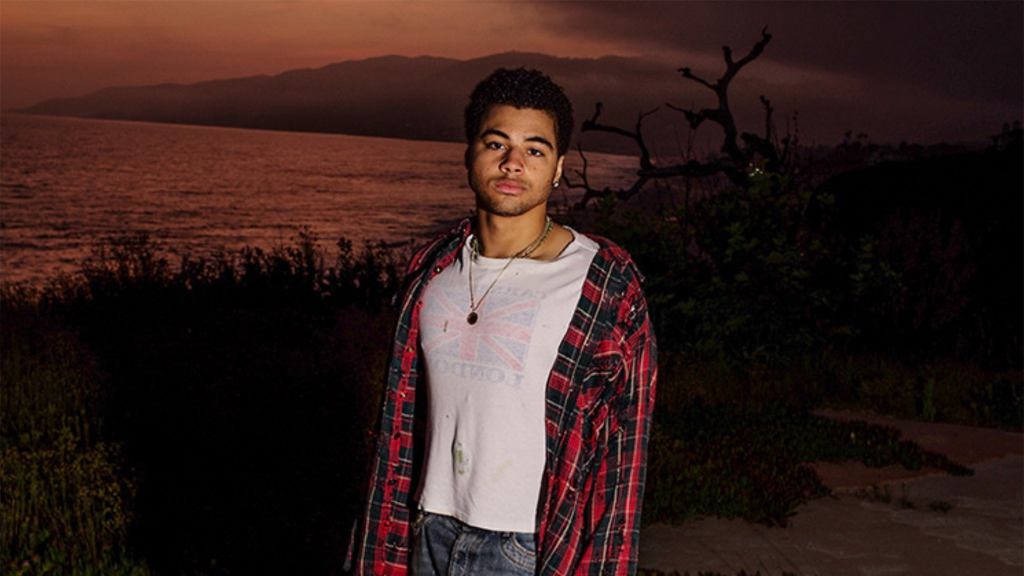 A young African-American man standing by a lake during sunset.