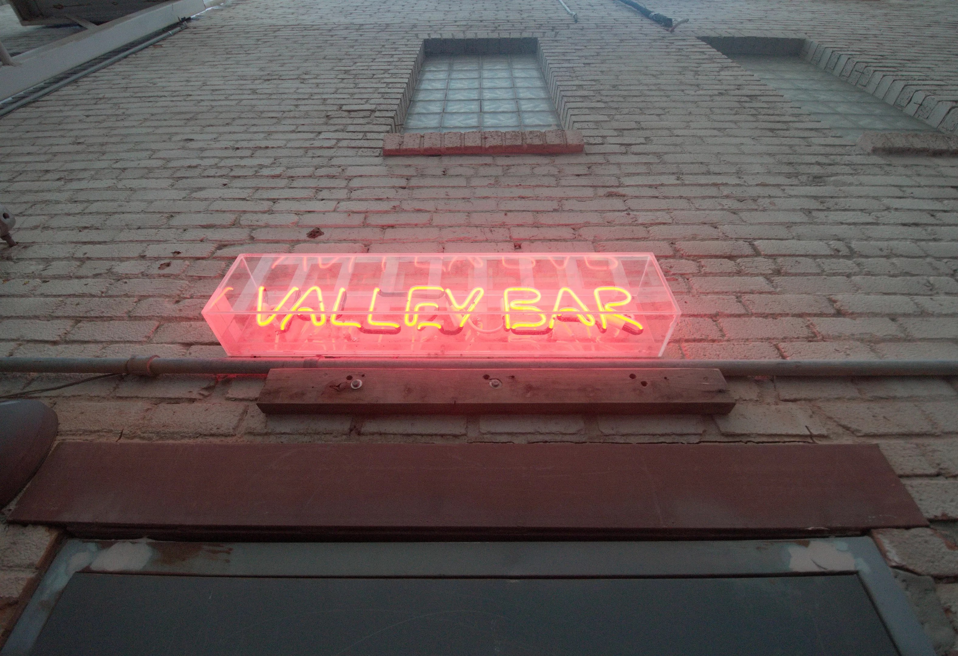 A neon sign on a brick wall above a door.