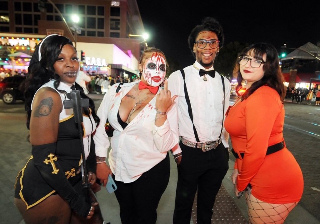 Four people dressed in Halloween costumes along a downtown street at night.
