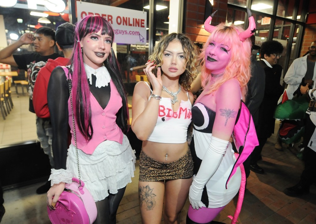 Three women in costume on a crowded sidewalk.