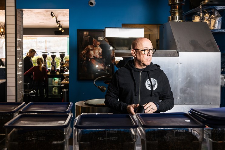 Bald man standing at a coffehouse counter.