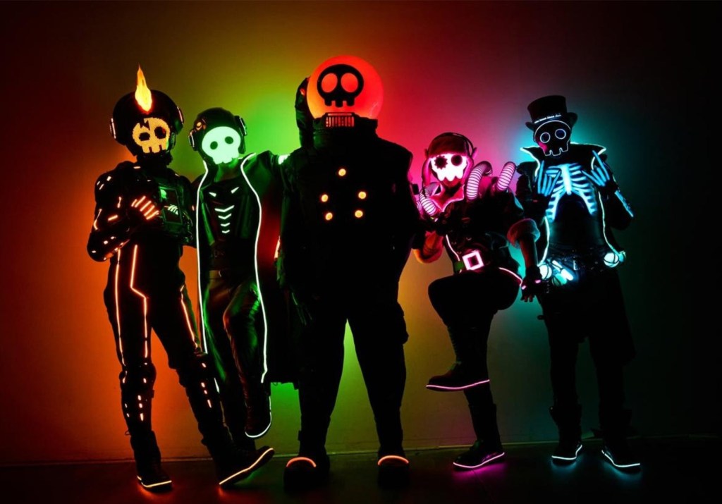 Five musicians in glowing multicolored costumes.