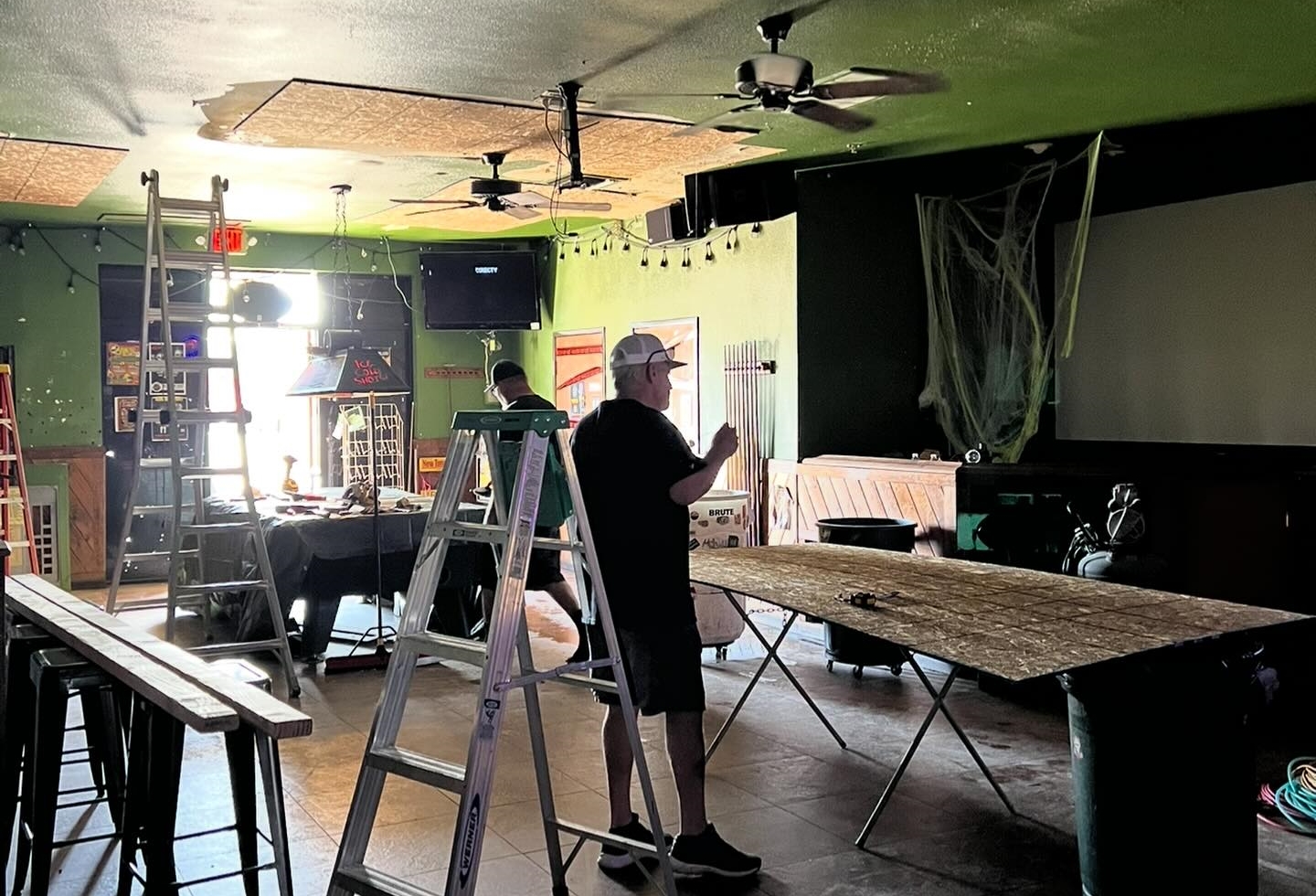 Two people conduct repair work amid ladders inside a bar,