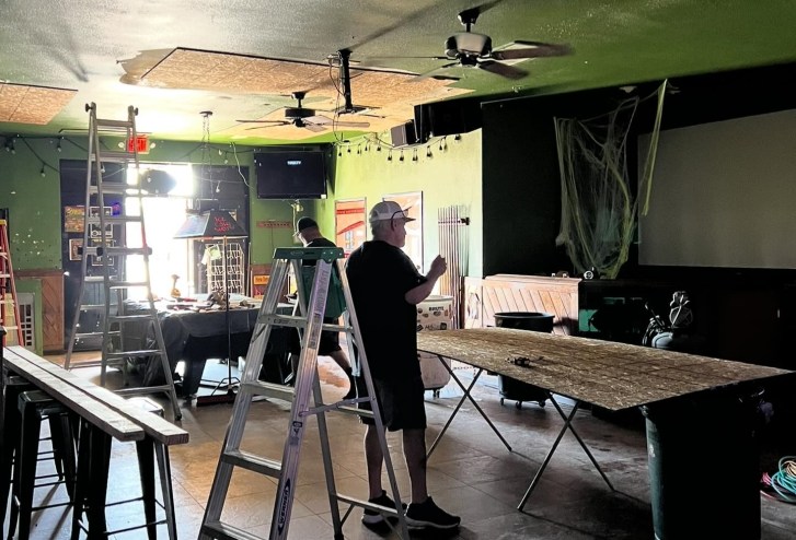 Two people conduct repair work amid ladders inside a bar,