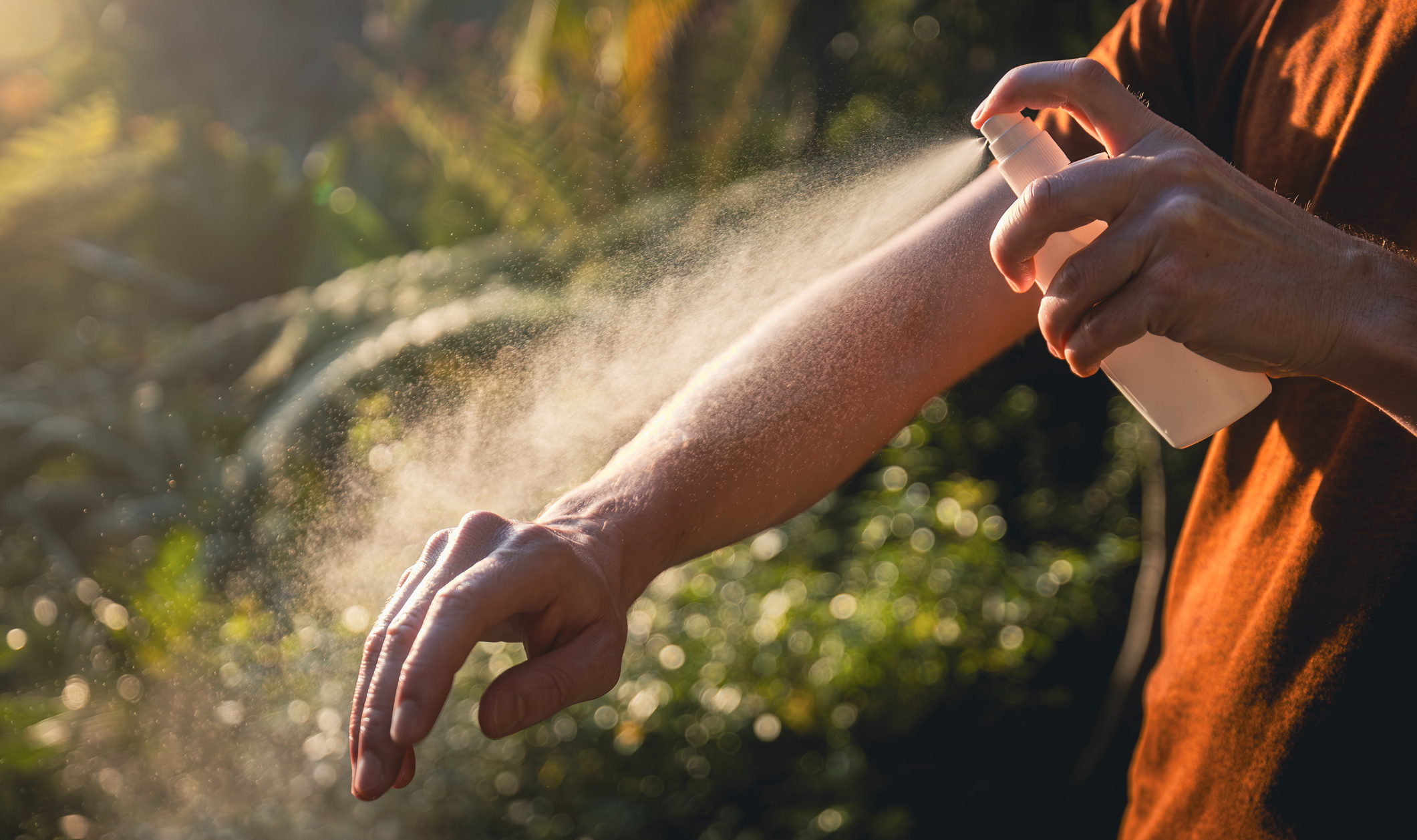 a person sprays bug spray on their arm