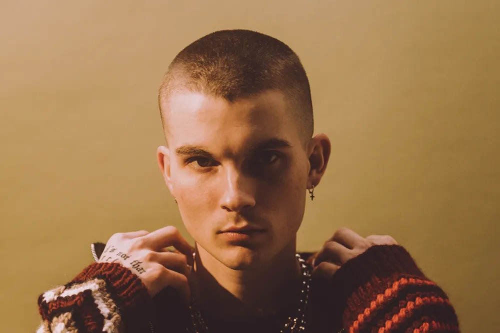 A younger man with a shaved head stares into the camera.