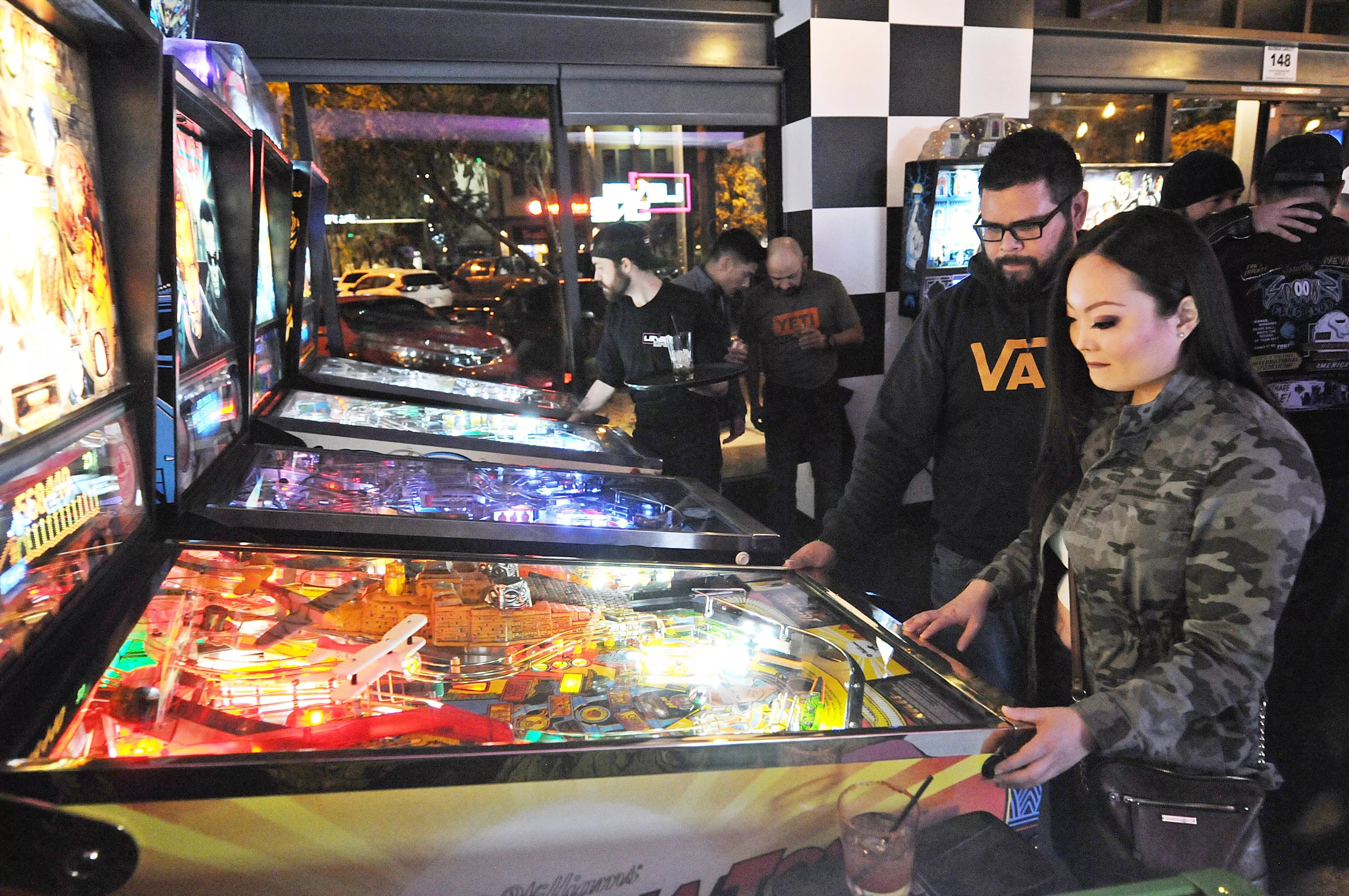 People playing pinball in an arcade.