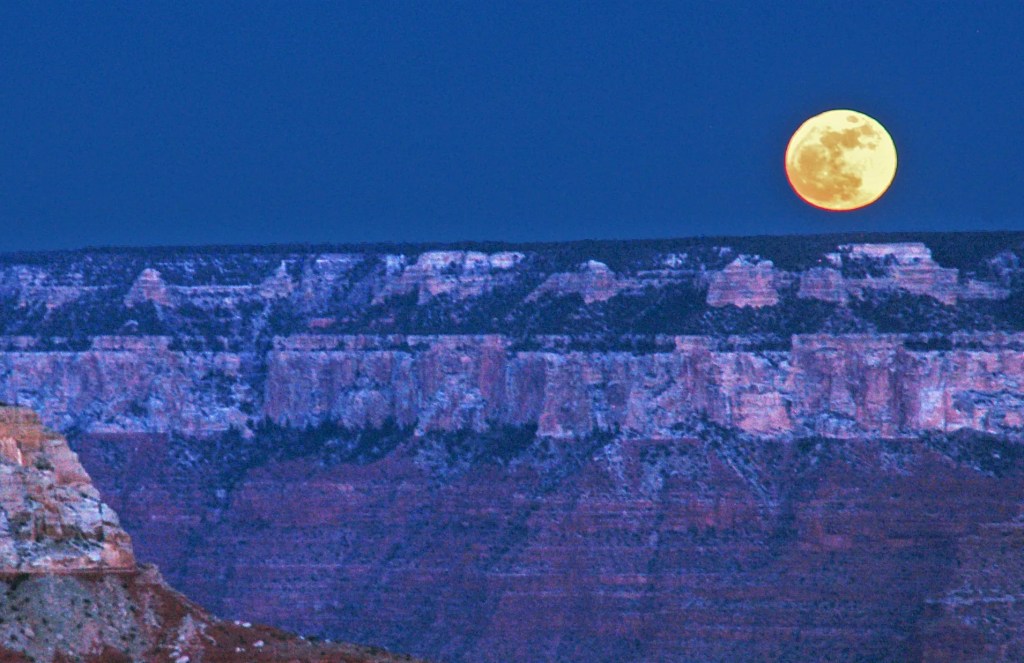 A large full moon rises over the Grand Canyon.