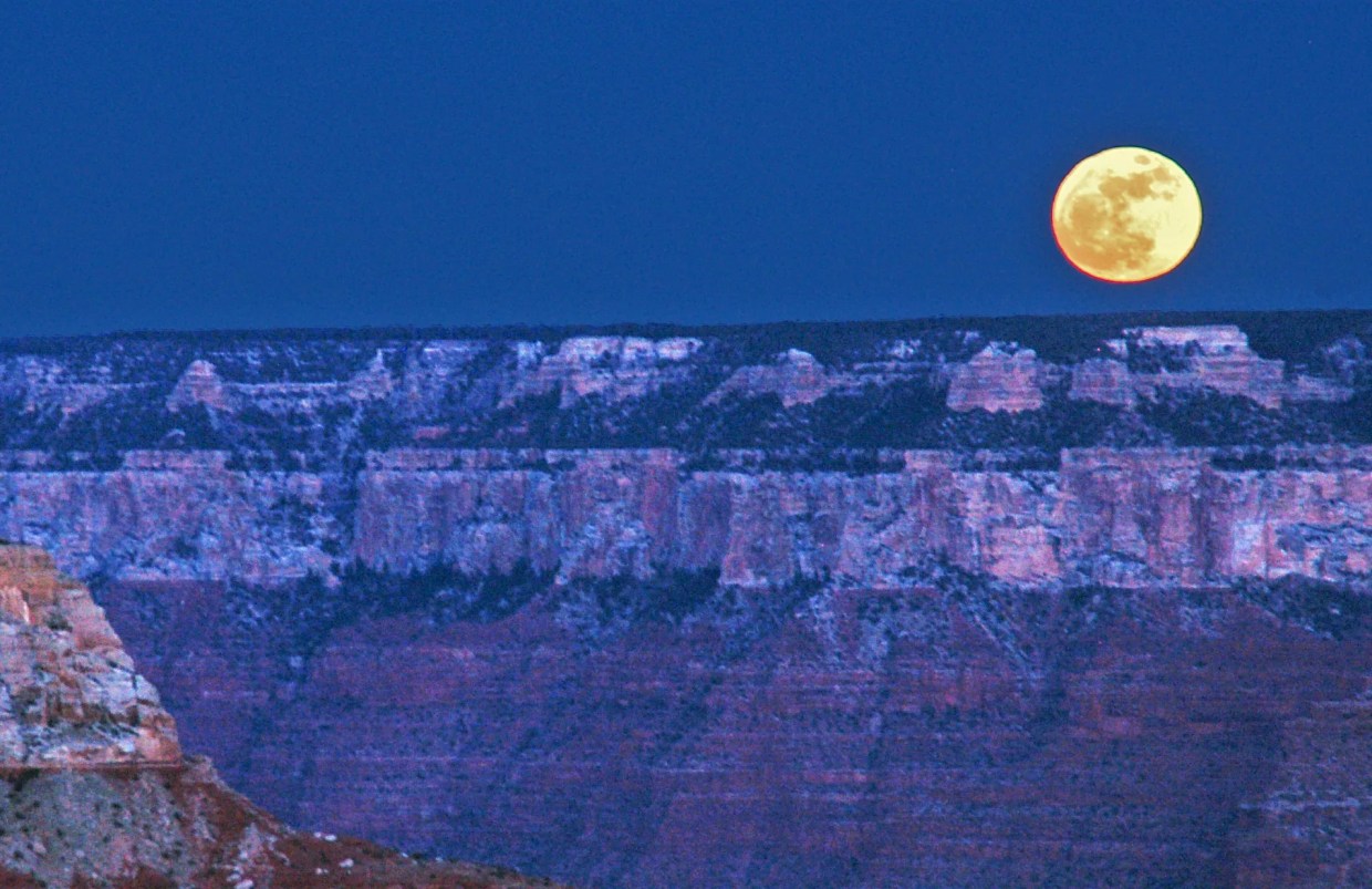 A large full moon rises over the Grand Canyon.