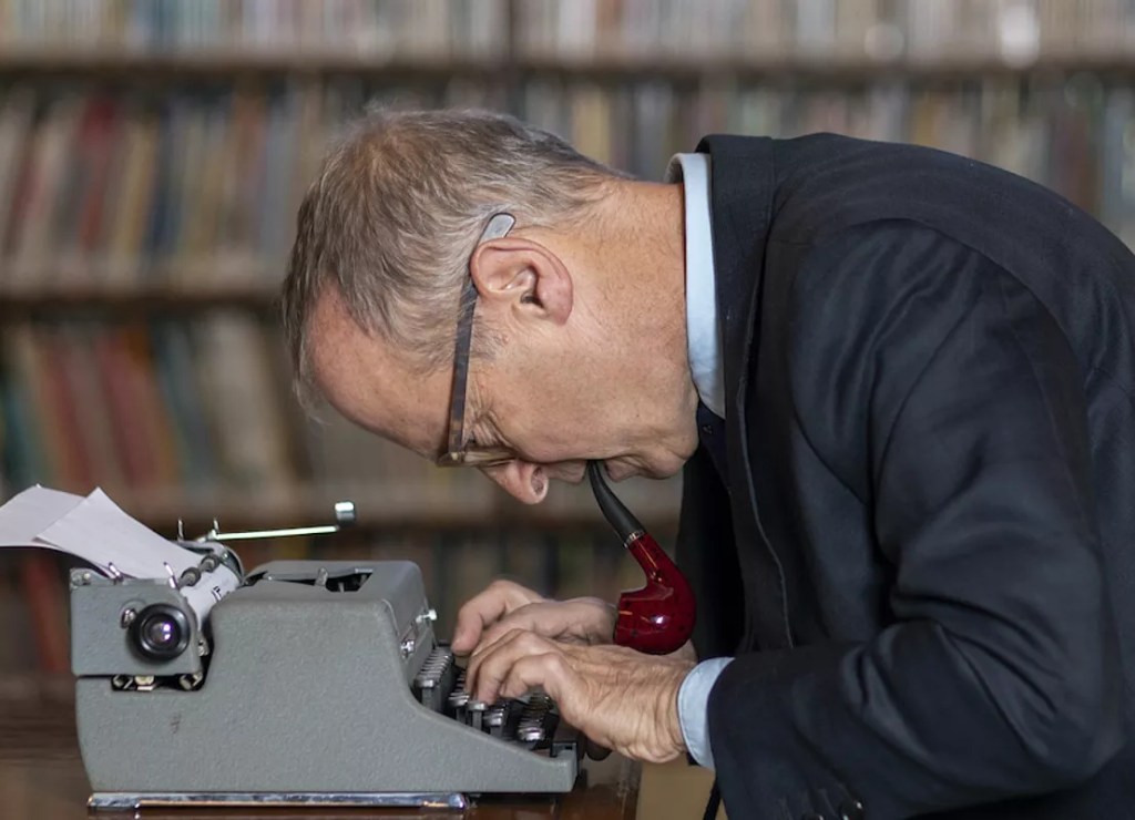 A middle-aged man in glasses looking closely at a typewriter.