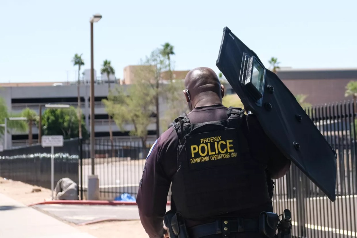 a phoenix police officer, seen from behind, holding a riot shield