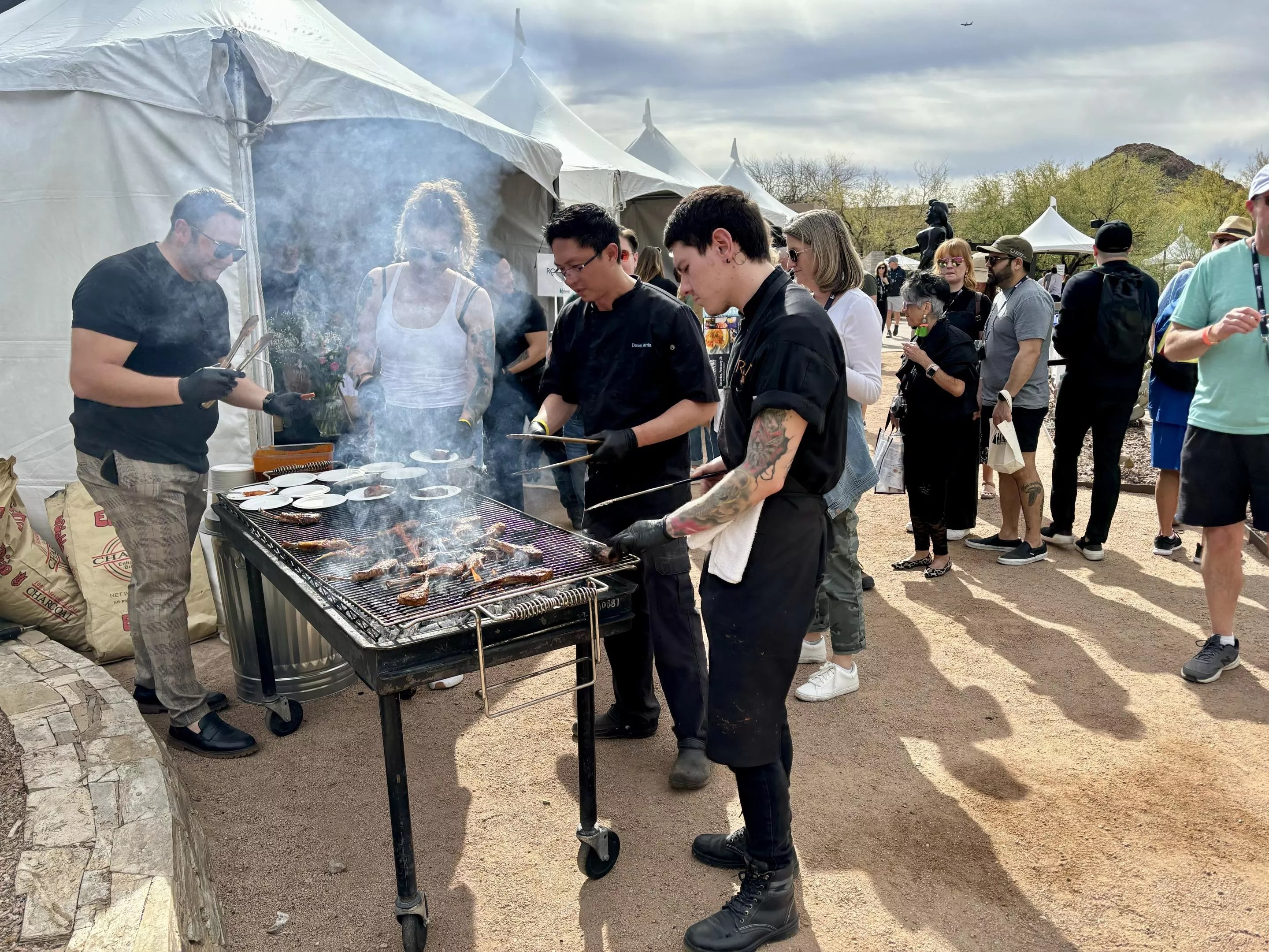 Smoking grill surrounded by waiting customers.
