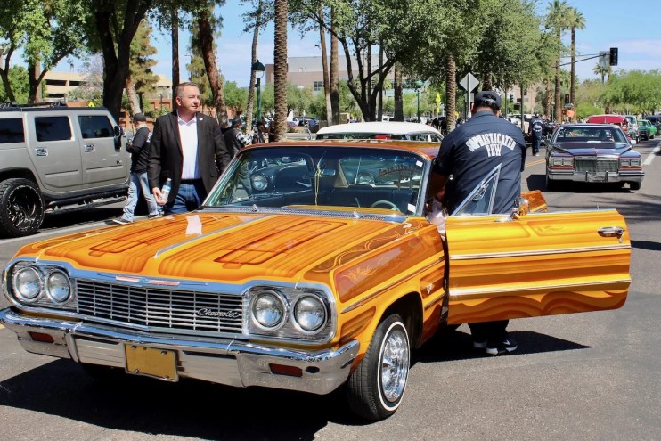 Two people get out of an orange lowrider car.