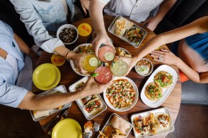 Clinking drinks over a table filled with plates of food.