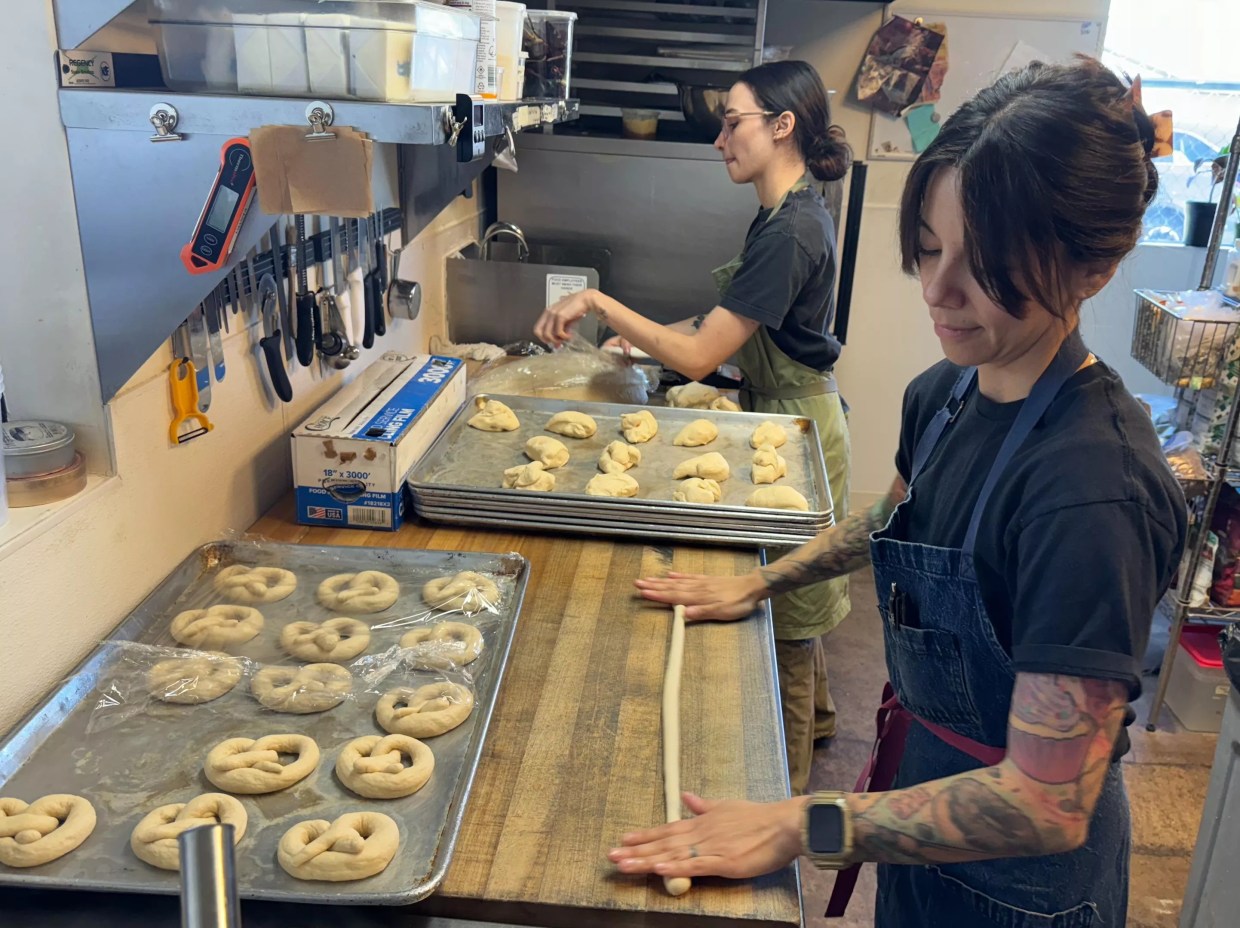 Two people roll out pretzel dough.