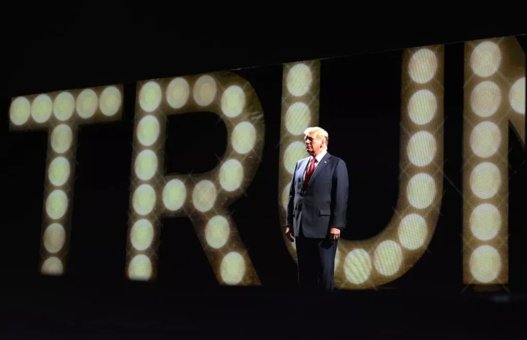 Donald Trump in front of a the name "Trump" in bright lights