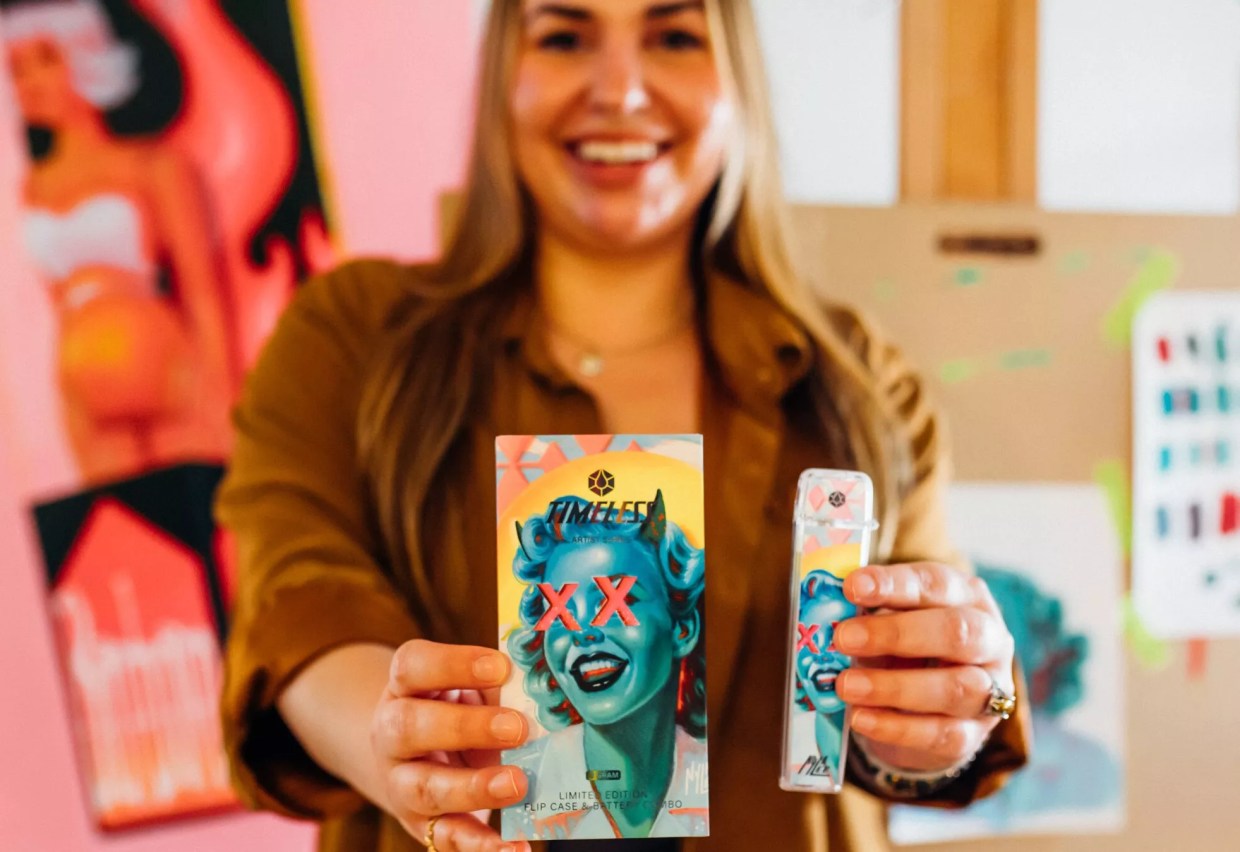 A woman in an art studio holding up a piece of art.