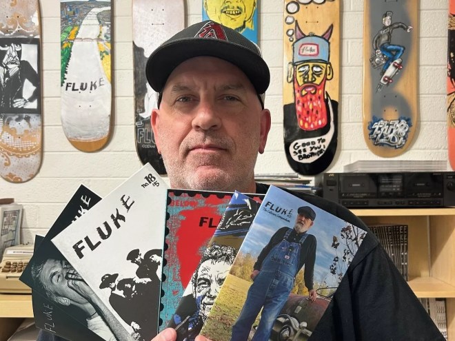 A man in a hat holding up a selection of zines.