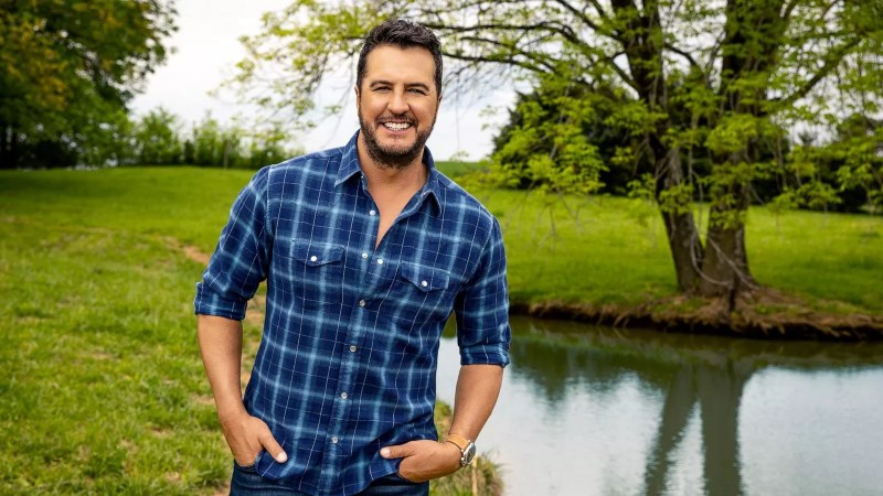 Man in a blue western shirt stands in front of a pond.