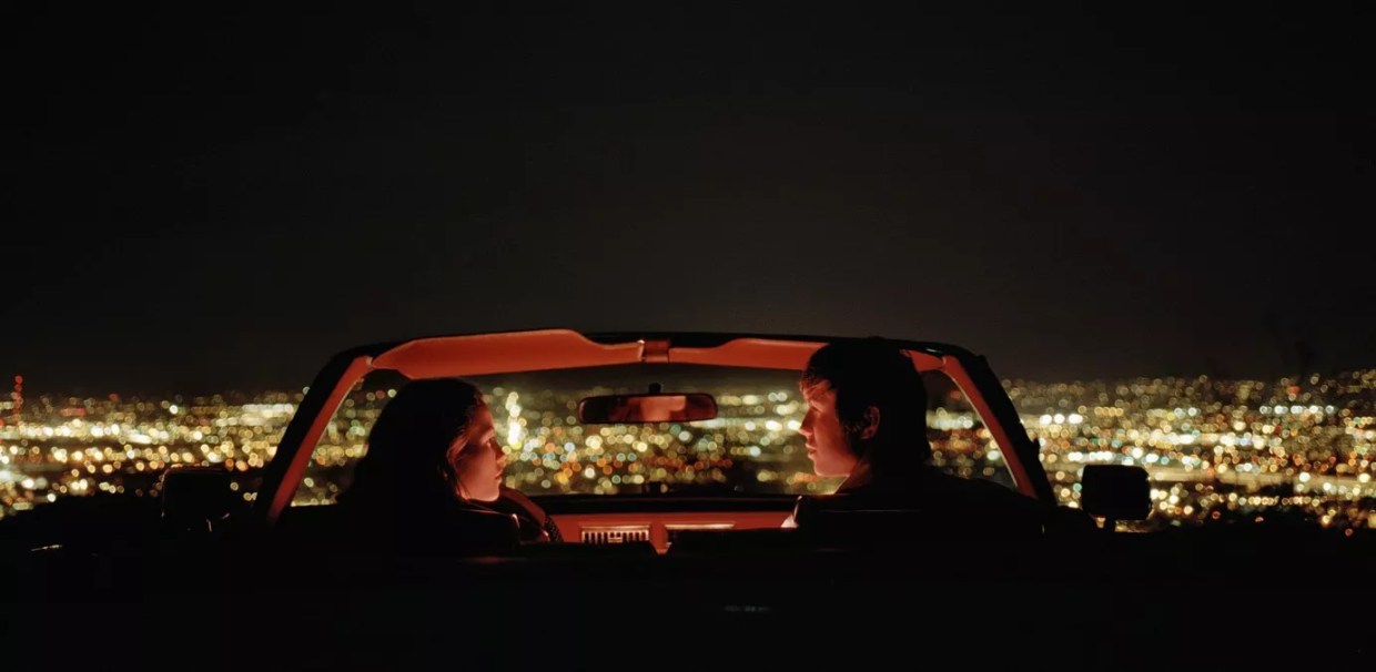 A couple in a convertible overlooking a city.