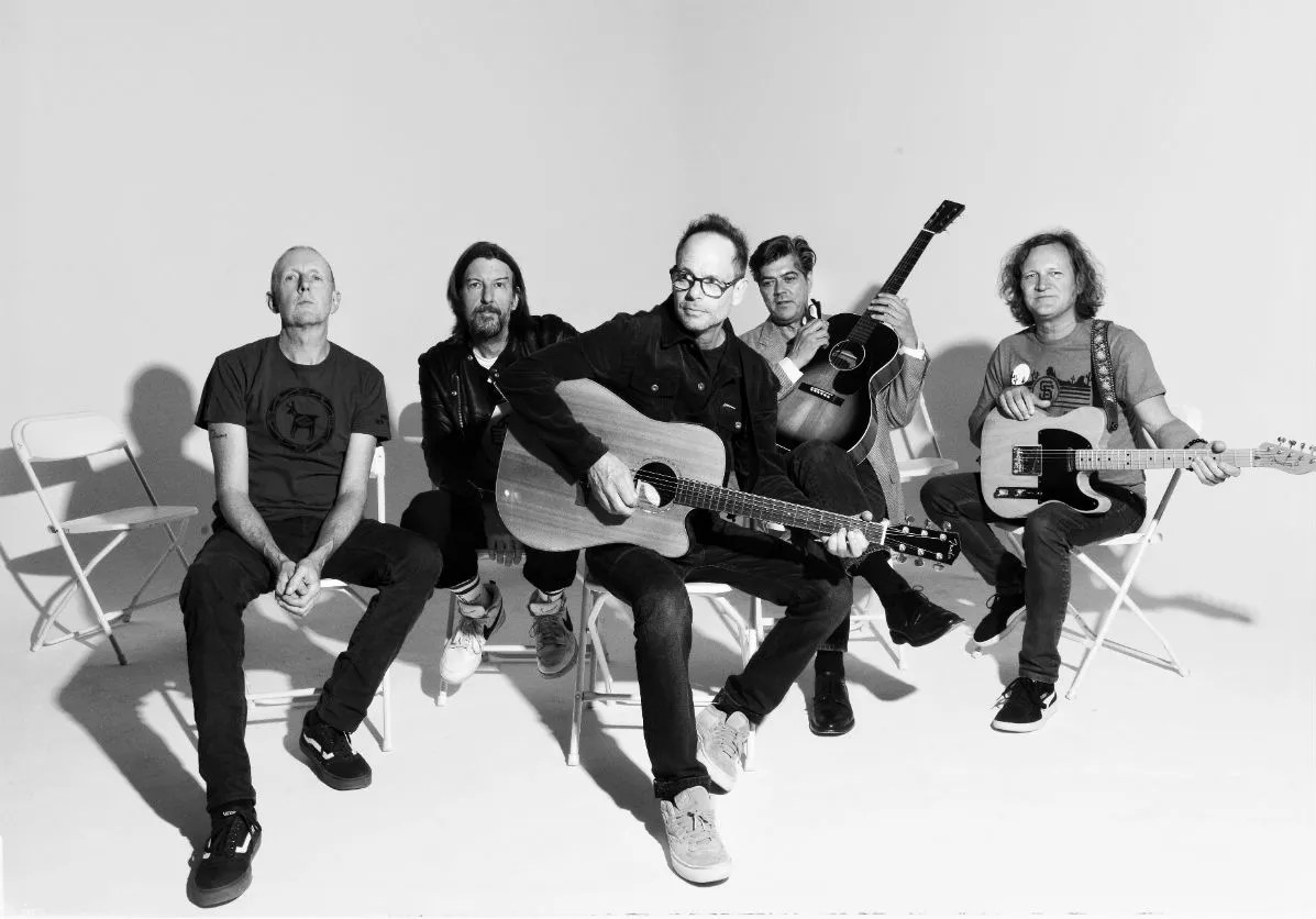 A rock band holding guitars while sitting on folding chairs.