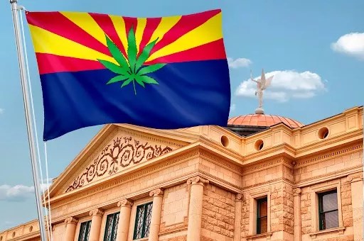 an arizona flag with a marijuana leaf on it flies in front of the Arizona capitol