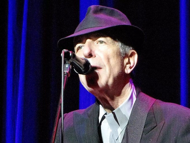 A man in a porkpie hat sings into a microphone.