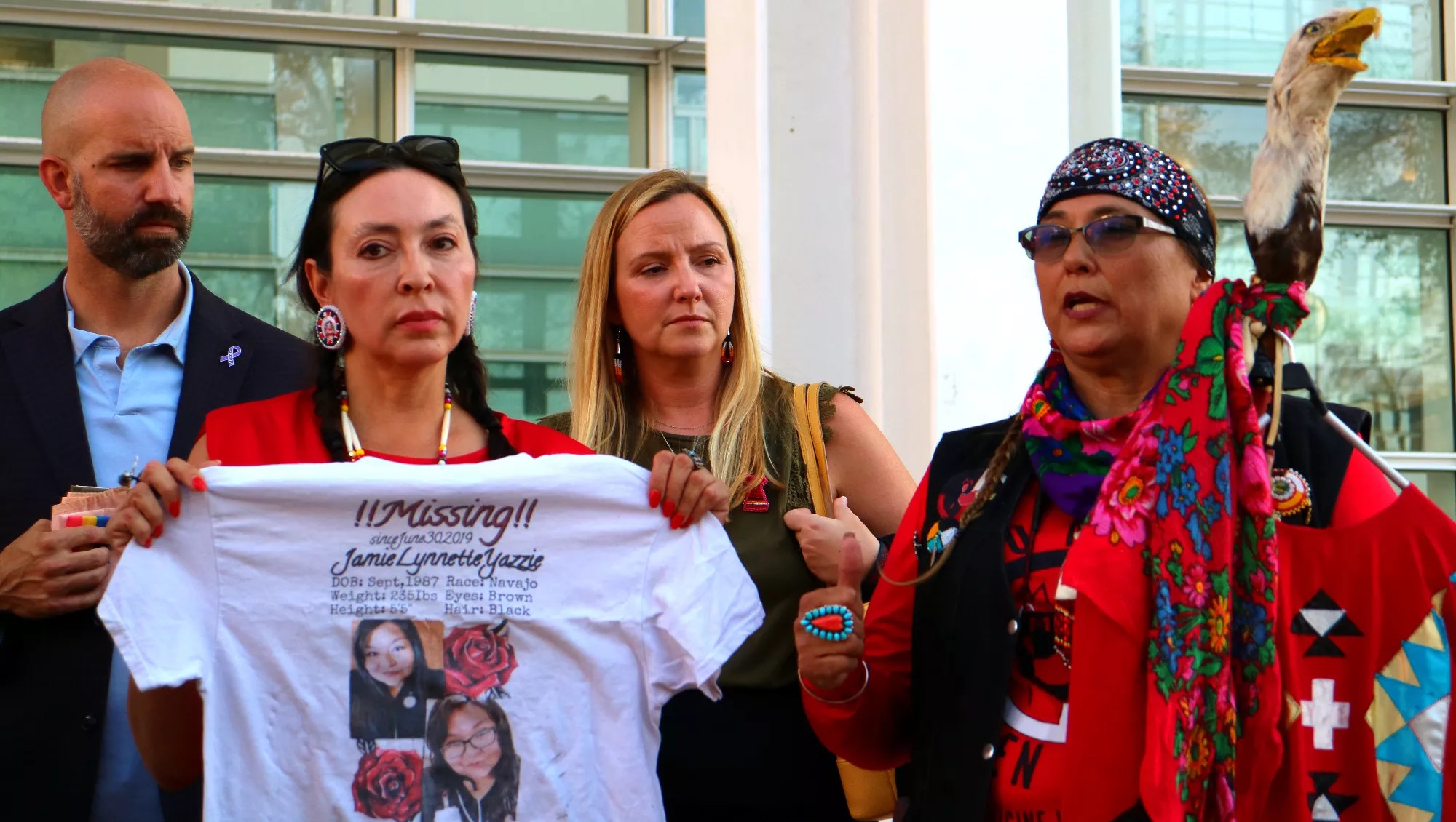 One woman holds a t-shirt spread out while another woman speaks with a man and a woman standing behind them.