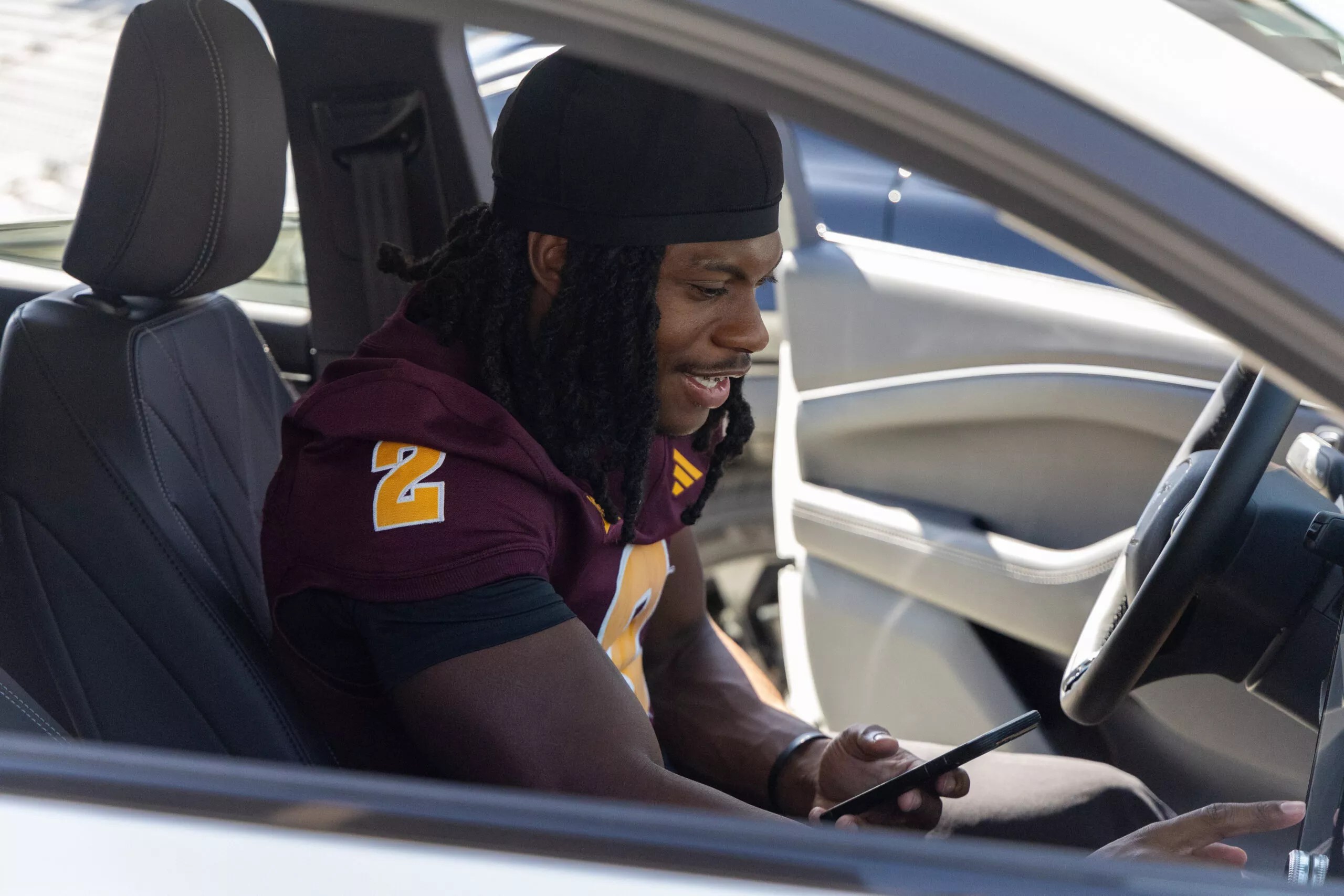 a young man in an ASU jersey sits in the front seat of a car