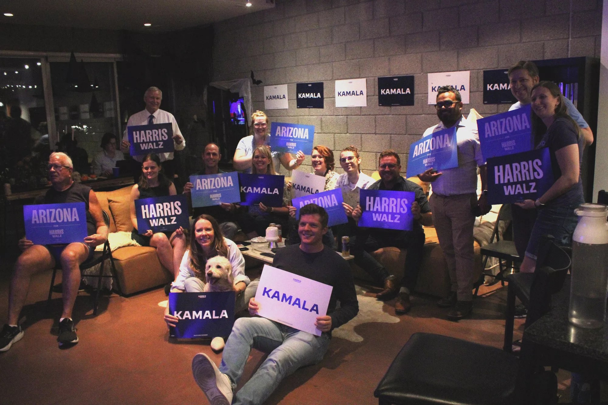 Guests for the LDS Advisory Committee Vice Presidential Debate watch party pose for a photo while holding Harris-Walz campaign signs