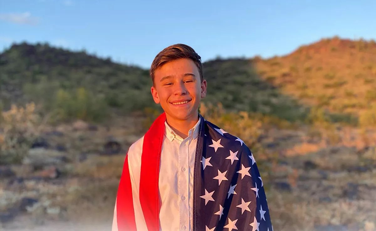 a baby-faced teen boy draped in an American flag