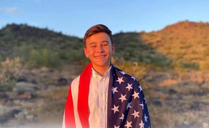 a baby-faced teen boy draped in an American flag