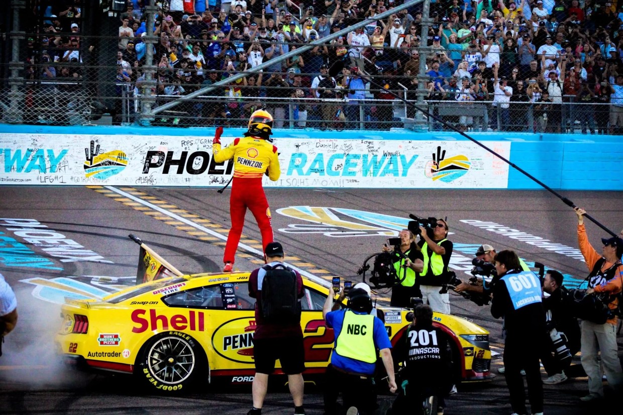 A racecar driver celebrates on a racetrack.