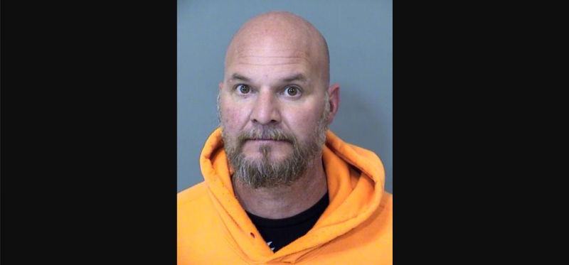 a bald man with a goatee in an orange hoodie seen in a mugshot