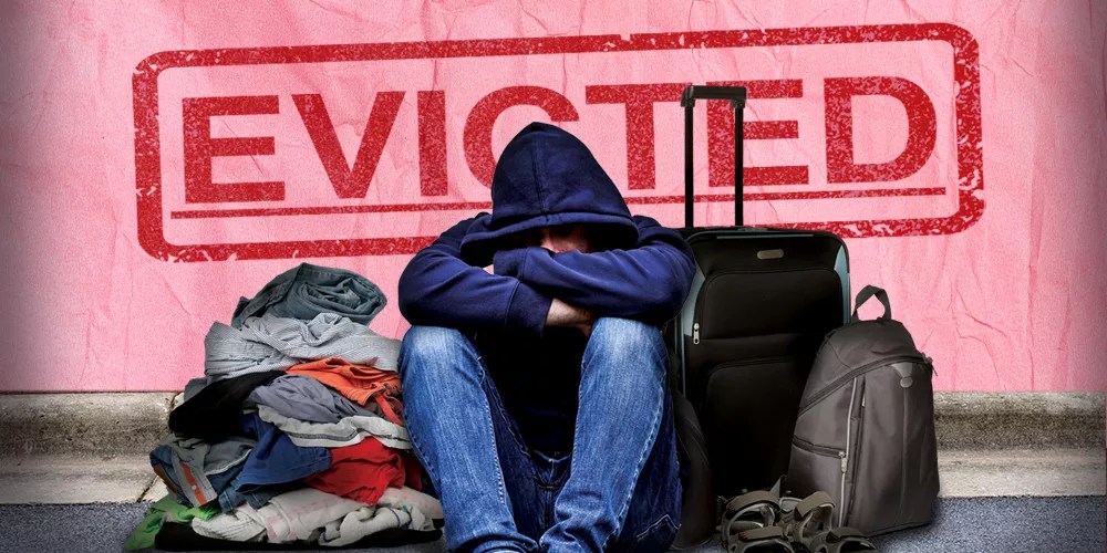 a person in a hoodie sitting depressed with luggage and clothes on the curb, with a superimposed eviction notice behind