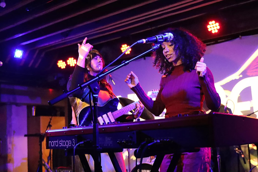 A guitarist and keyboard player performing onstage a concert venue.