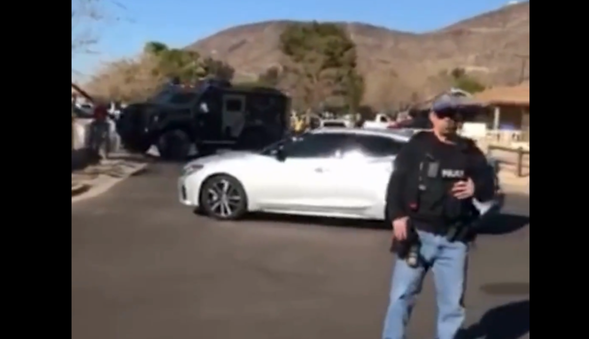 an ICE agent with a rifle stands in front of an unmarked car and an armored truck