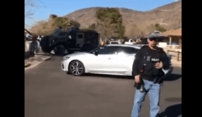 an ICE agent with a rifle stands in front of an unmarked car and an armored truck