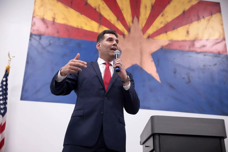 rodney glassman speaks in front of an arizona flag background
