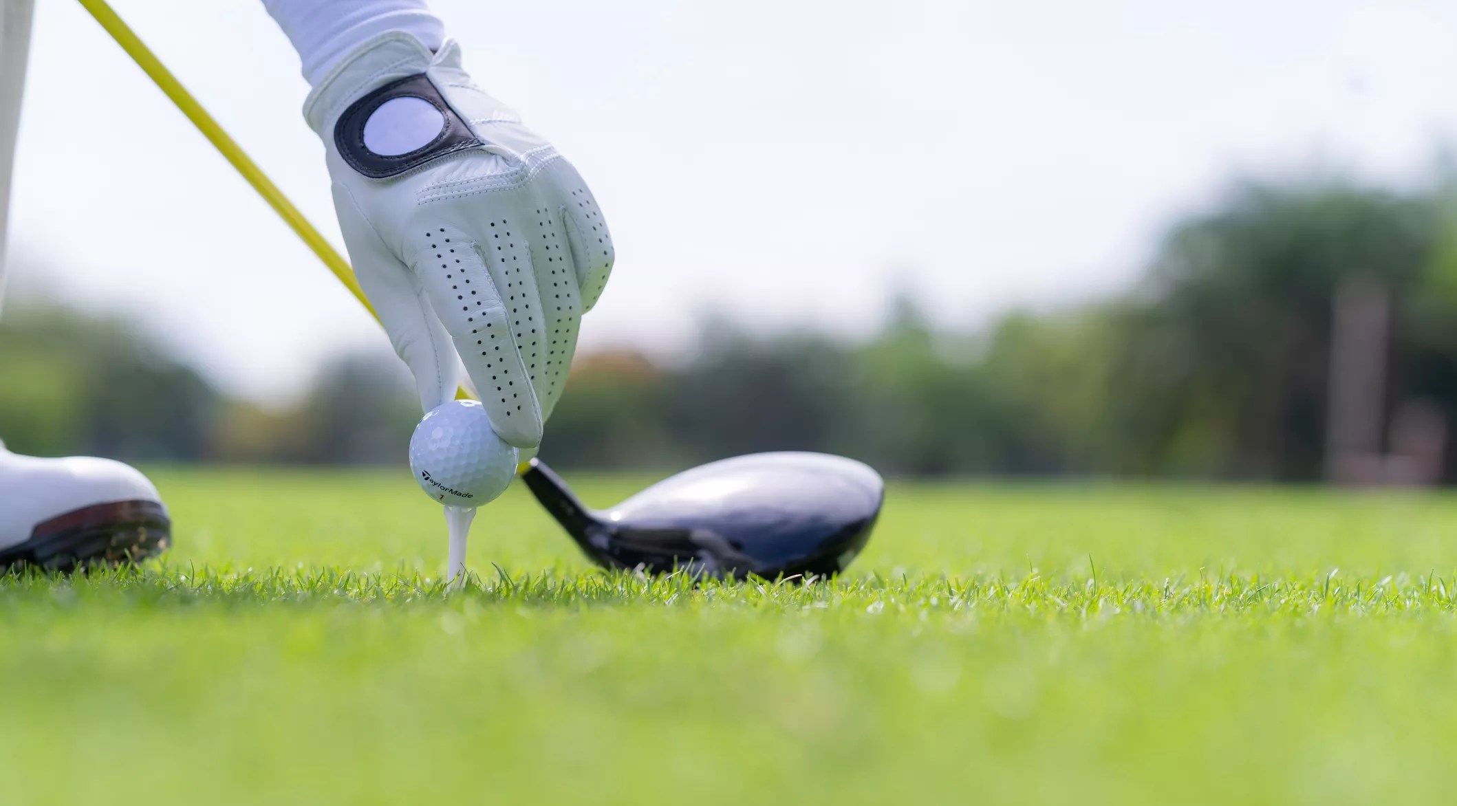 a gloved hand placing a ball on a tee in front of a golf club