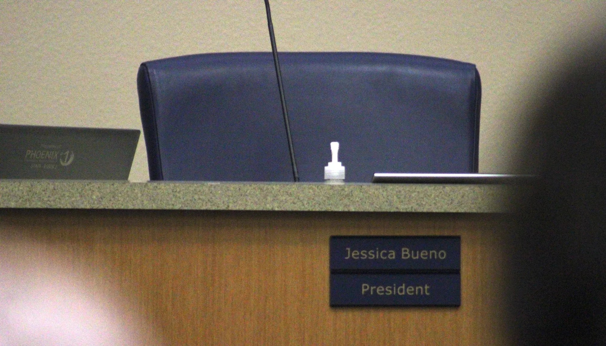 an empty chair at a public meeting with a "jessica bueno" placard