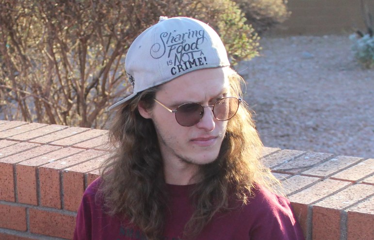 a young man in a backward hat that says "sharing food is not a crime"