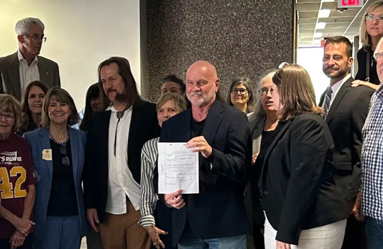 a man holds up a sheet of paper surrounded by other people