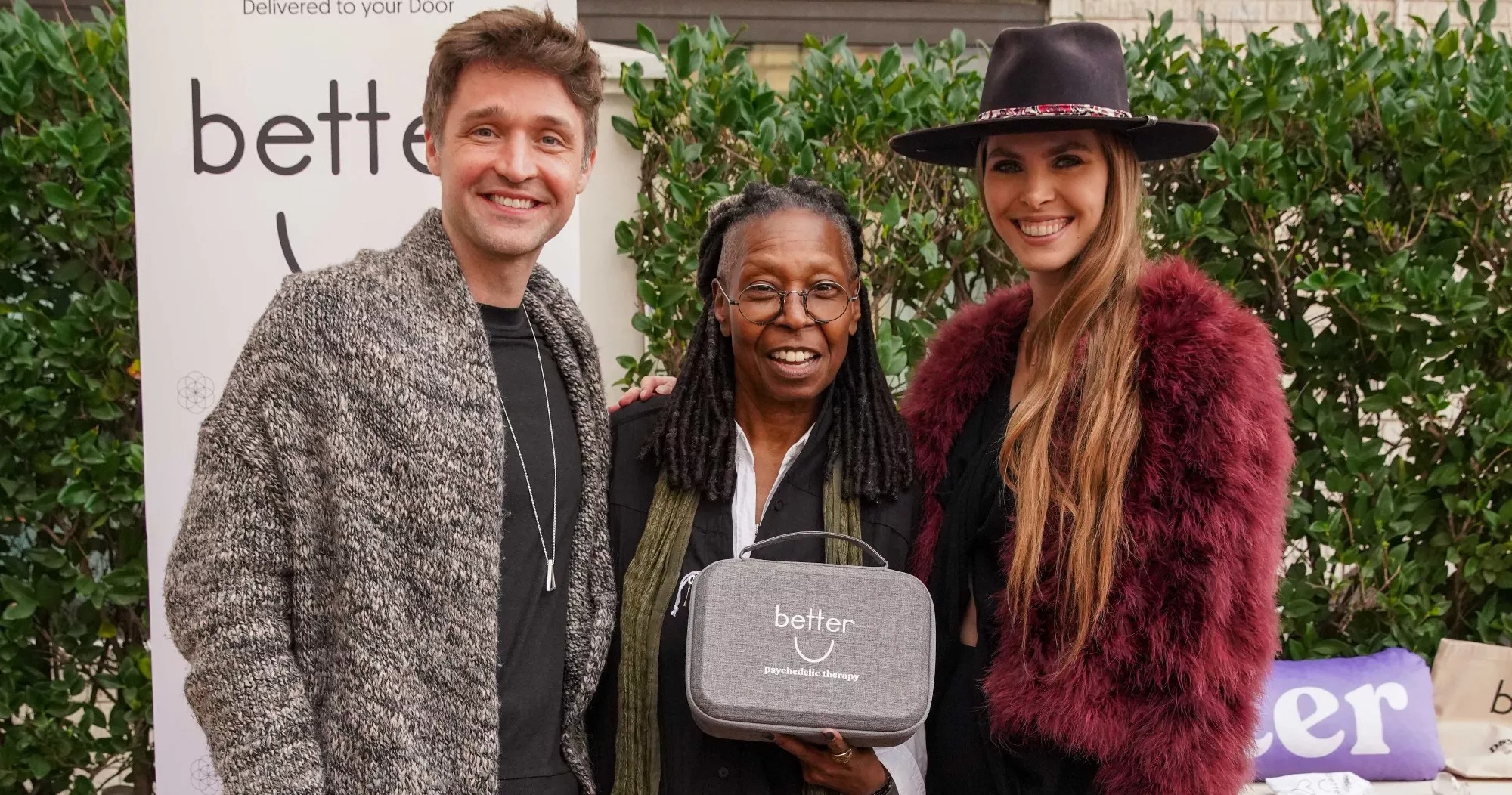 a man and woman pose with whoopi goldberg, who is holding a gray pouch that says "Better U"
