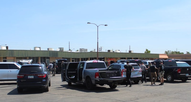 a bunch of unmarked law enforcement vehicles in a parking lot, with people milling about