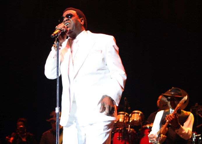 An African-American vocalist dressed in white sings into a microphone.
