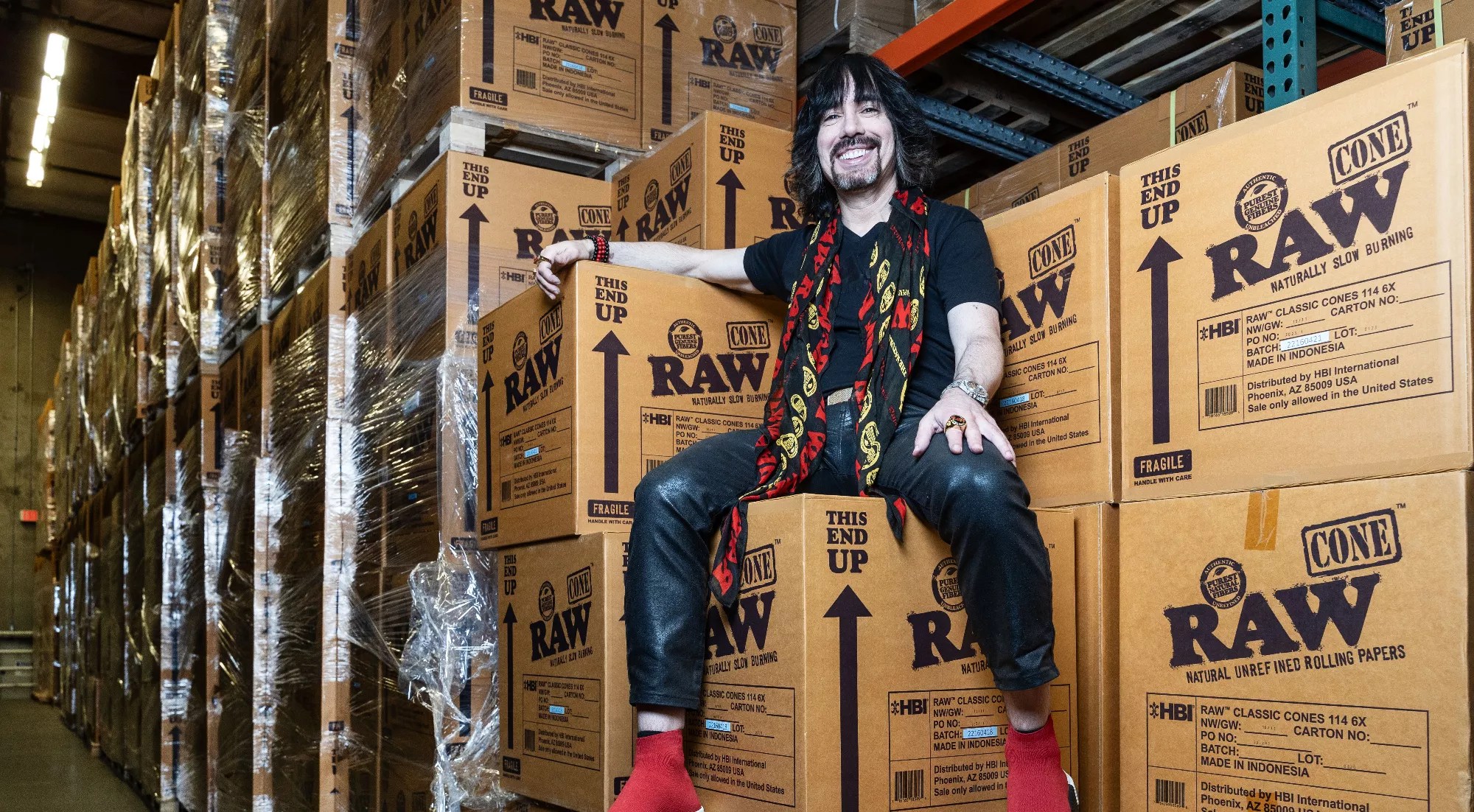 a man in a black shirt and red scarf sits on a pile of boxes